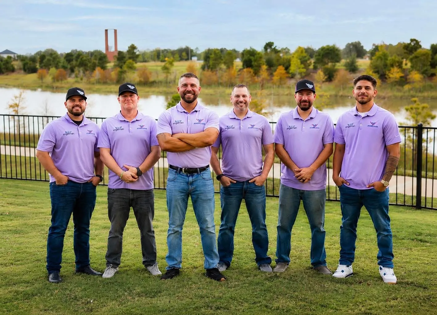 The Angelman Roofing & Restoration team in matching branded polos, standing together on a lawn beside a lake